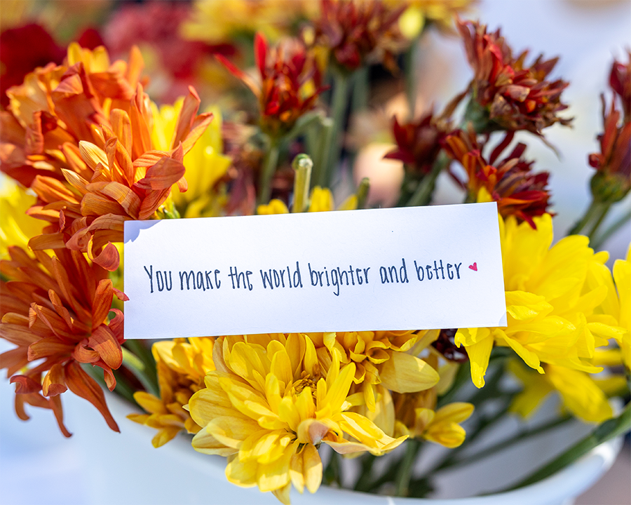 A handwritten note placed in orange flowers reads "you make the world brighter and better"