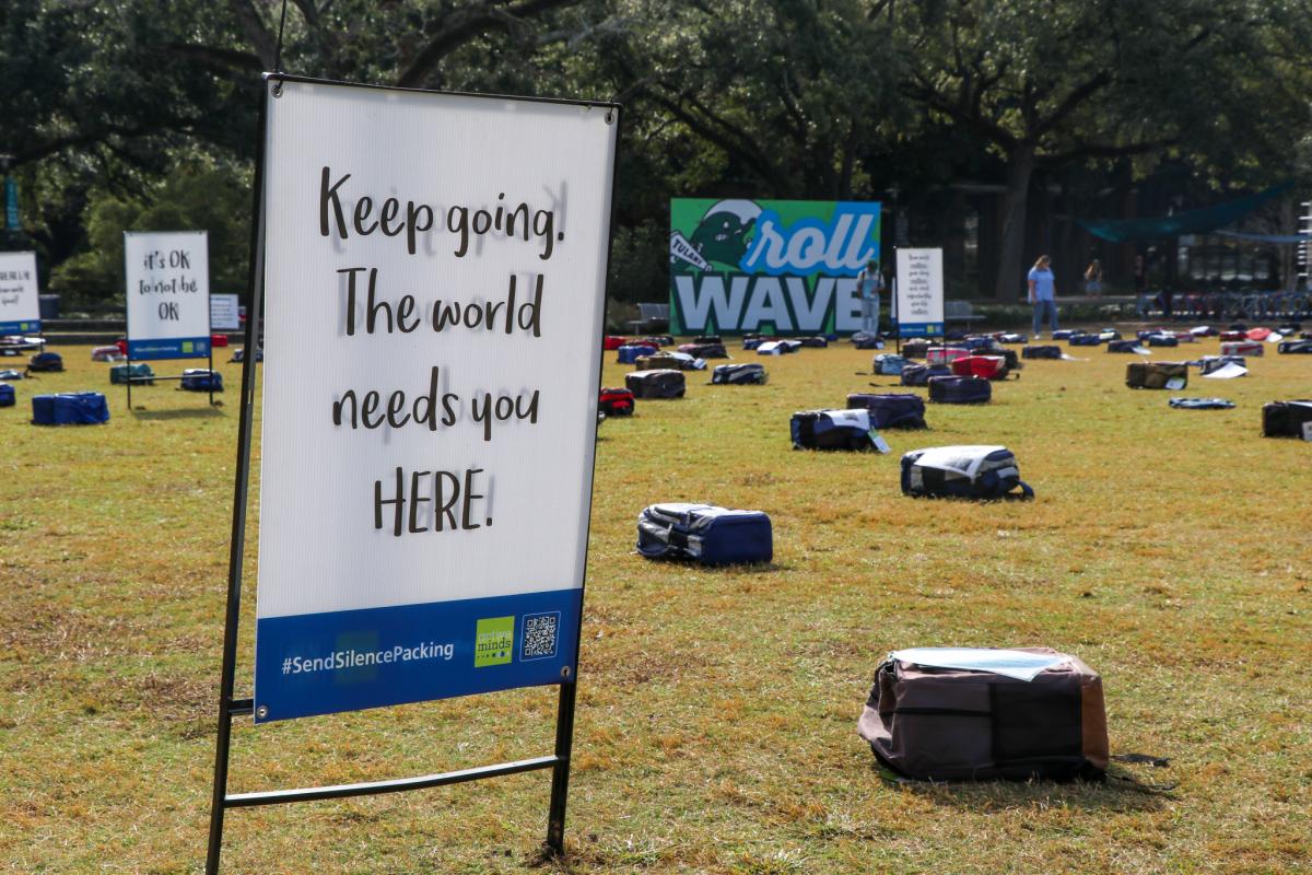 a sign reads "keep going, the world needs you here!" in front of an installation of hundreds of backpacks on the Berger Family Lawn representing those lost to suicide each year